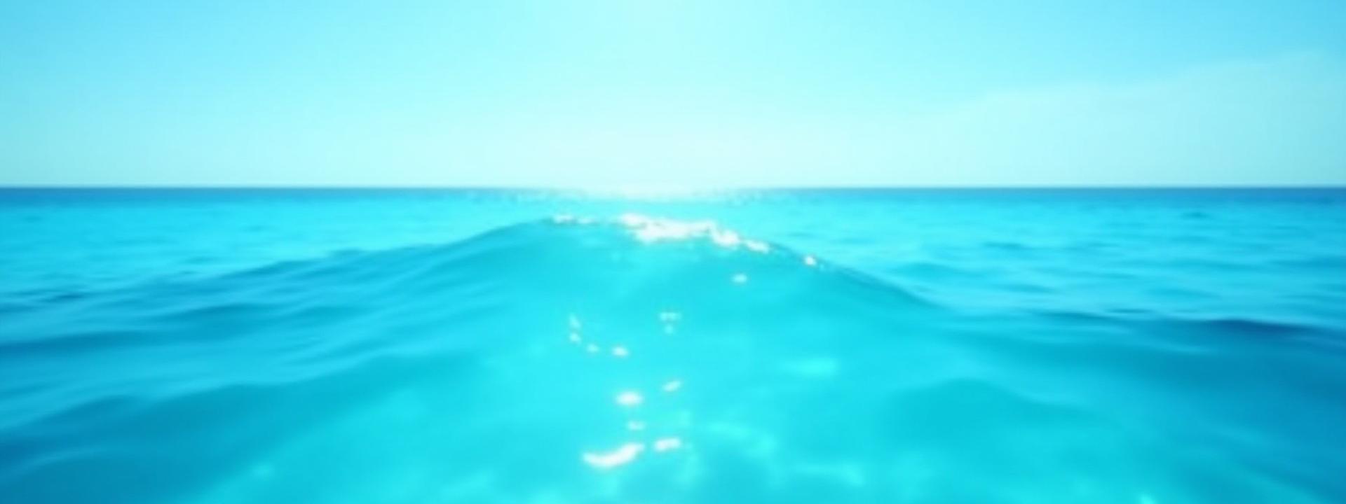 Clear, pristine ocean water shimmering under the sun, a clean wave breaking gently in the distance